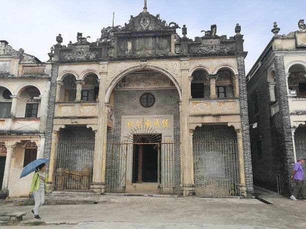 Woman with umbrella stands in front of ancestral hall in Cangdong Village, China