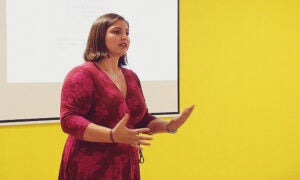 woman in red dress giving presentation in front of a yellow wall