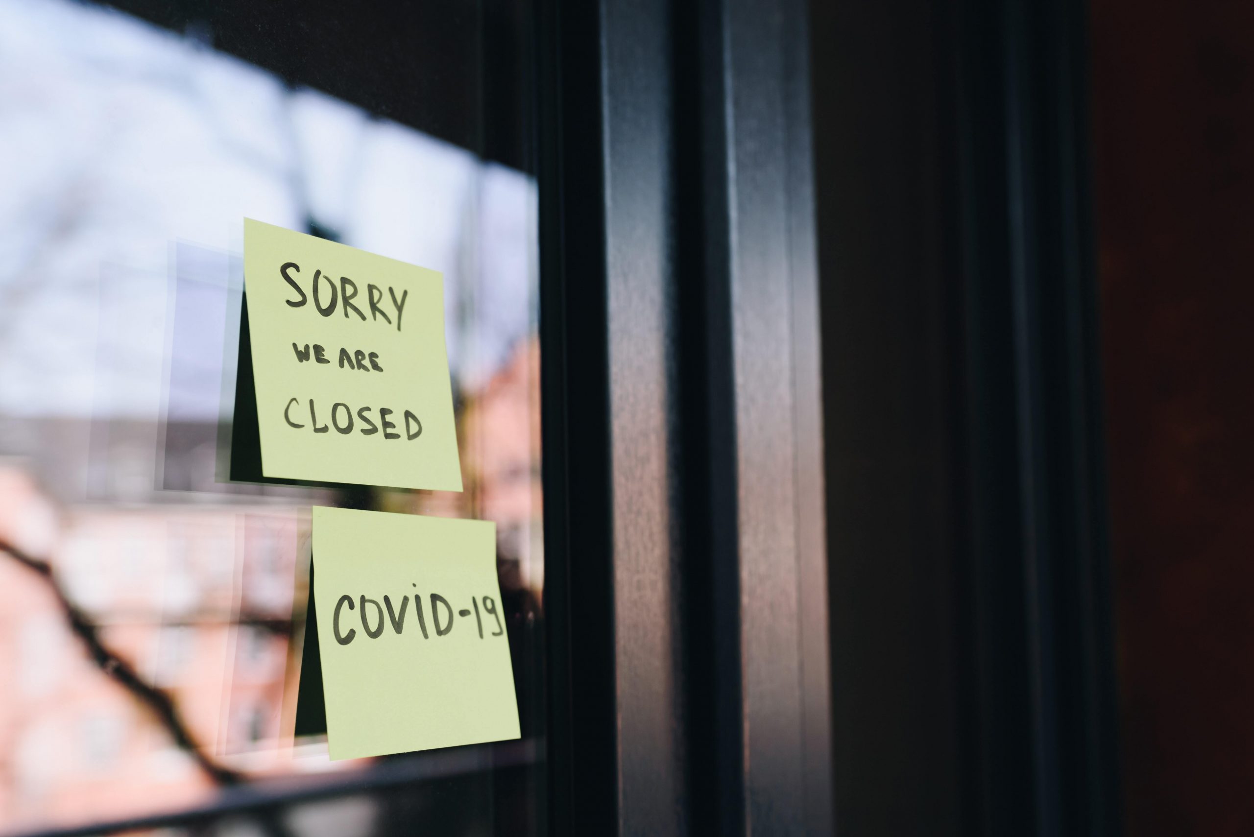 A handwritten post-it note on the window of a business reads "Sorry we are closed. COVID-19."